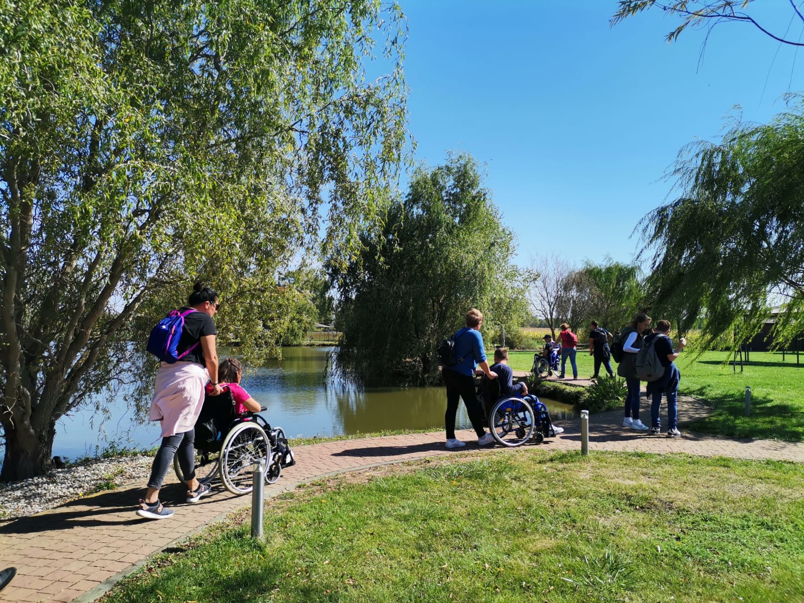 Osobe u invalidskim kolicima u pratnji svojih asistenata idu oko jezera